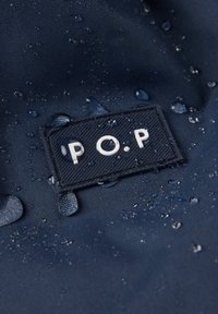 Marine vandtæt stof med et syet mærke med hvide bogstaver "P.O.P." Vanddråber er synlige på overfladen, hvilket fremhæver teksturen.