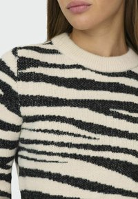 Black and white striped sweater with a ribbed round neckline, made from soft knit fabric, featuring varying stripe thickness.