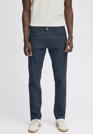 Marineblå bomullsblandingsbukser med rett ben-design, med frontlukking med knapp og sidelommer, iført med hvite sneakers.