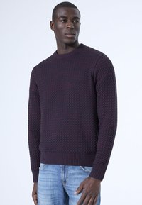 Marineblauwe gestructureerde gebreide trui met een ronde hals en geribde manchetten, gecombineerd met lichtblauwe jeans. Bevat een gezellige, geweven patroon.