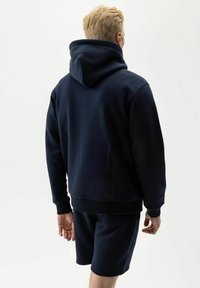 Navyblauwe hoodie gemaakt van zacht materiaal, met een kangoeroezak en geribbelde manchetten, gecombineerd met bijpassende shorts.