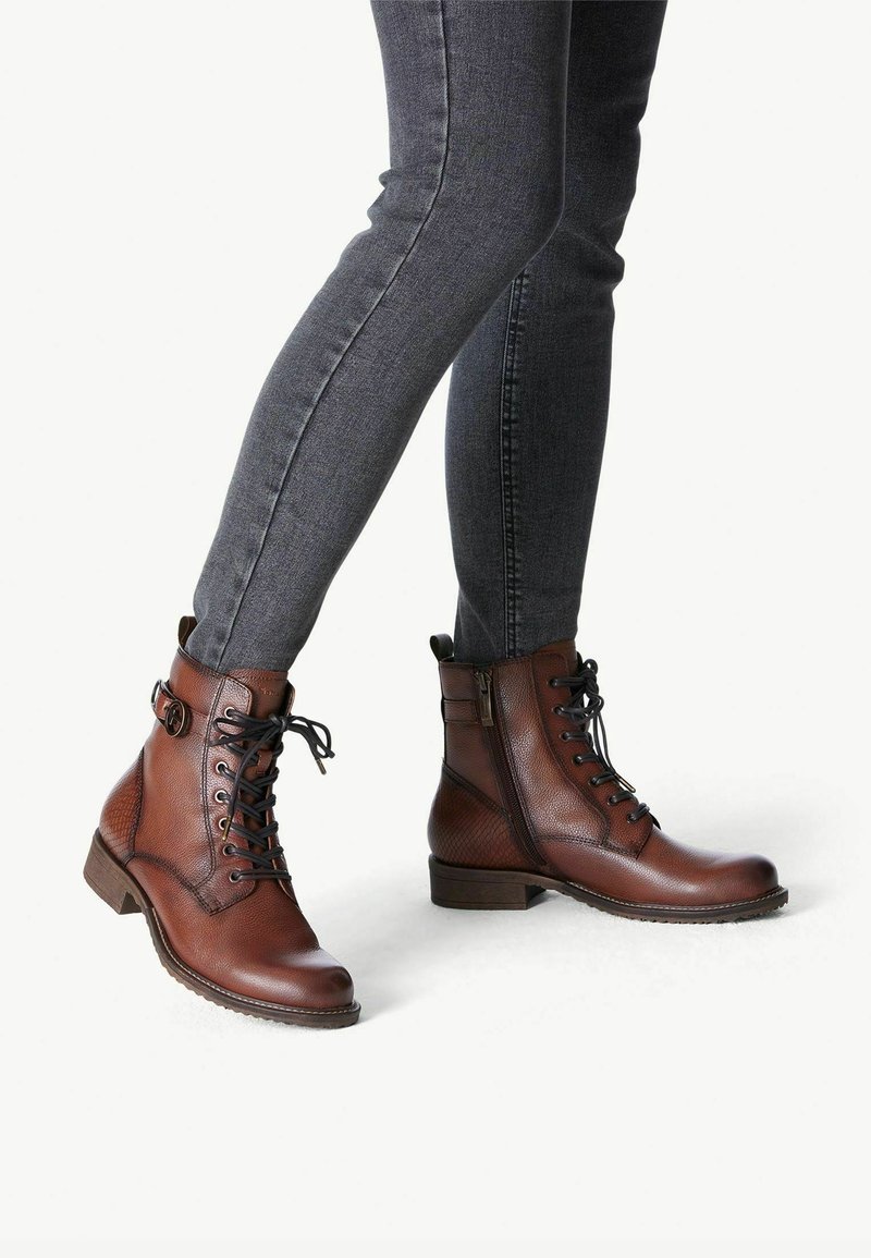 Bottes chelsea en cuir marron avec lacets, fermeture éclair latérale et motif texturé. Présentent un talon bas et un bout rond pour le confort.