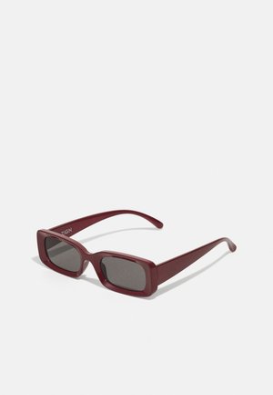 Burgunderfarbene rechteckige Sonnenbrille mit dunklen Gläsern, dicken Fassungen und schmal zulaufenden Bügeln. Hergestellt aus glänzendem Kunststoff mit glatter Textur.