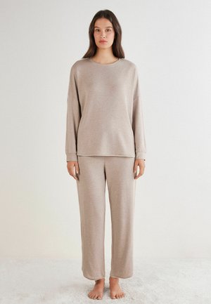 Helles beiges Lounge-Set bestehend aus einem langärmeligen Oberteil und lockeren Hosen aus weichem Stoff, mit dezenten Nähdetails an den Säumen.