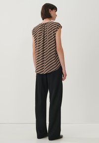 Korte mouwen bruine blouse met geometrische patronen, gecombineerd met zwarte wijde broek. Zachte stof met een relaxed fit.