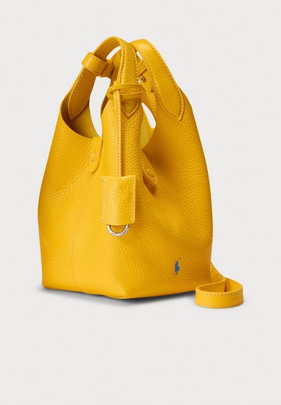 Mala žuta kožna torba u obliku kantice s teksturiranim završetkom, s gornjom ručkom, uklonjivim remenom za rame i plavim detaljem logotipa.