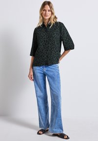 Sort og grøn leopardprint skjorte med korte ærmer, knaplukning foran, parret med lyseblå flared jeans og sorte sandaler.