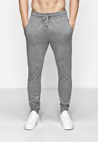 Grå sweatpants lavet af blødt stof, med en snoretræk i taljen, sidelommer og en tætsiddende pasform, parret med hvide sneakers.