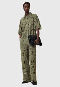 Olivengrünes Spitzen-Zweiteiler-Set mit floralen Ausschnitten, bestehend aus einem kragenlosen, knöpfbaren Hemd und passenden weiten Hosen. Schwarze, strukturierte Clutch-Tasche.
