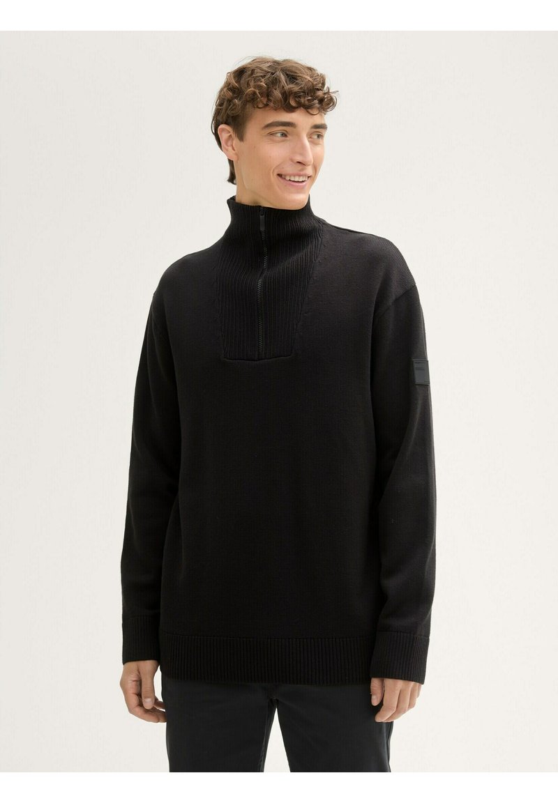 Schwarzer Pullover aus Strickstoff, mit einem hohen Kragen und einem halben Reißverschluss, gerippten Bündchen und einer Schulterpasse.