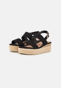 Sandalias de plataforma negras con suela de yute trenzado, que presentan tiras entrelazadas y una hebilla ajustable en el tobillo. Textura suave similar a ante.