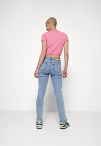 Top rosa justo de mangas curtas combinado com jeans skinny azul claro. Os jeans apresentam um remendo de denim na cintura e um detalhe de costura subtil.