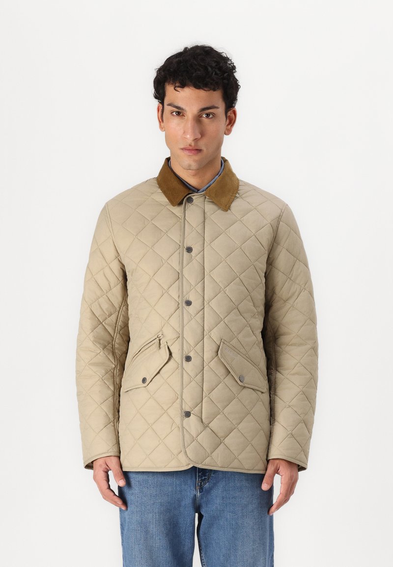 Beige gesteppte Jacke mit einem Cordkragen, Druckknöpfen und zwei Fronttaschen. Das Material ist glatt und hat eine Rautenstruktur.