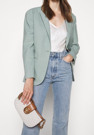 Femme portant un blazer vert clair, un haut blanc à col en V, un jean bleu taille haute, tenant un sac à main beige à motifs marron.