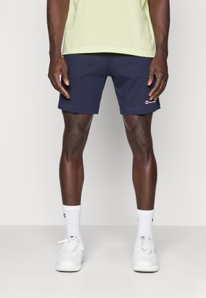 Marineblauwe sportshorts met een elastische tailleband, voorzien van een klein rood en wit logo flapje. Draag ze met witte sneakers en sokken.