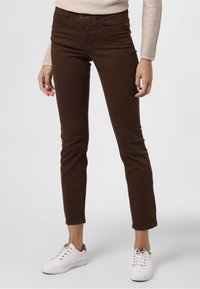 Hnědé slim-fit džíny s středním pasem, se zapínáním na zip a knoflík, předními kapsami a v kombinaci s bílými teniskami.