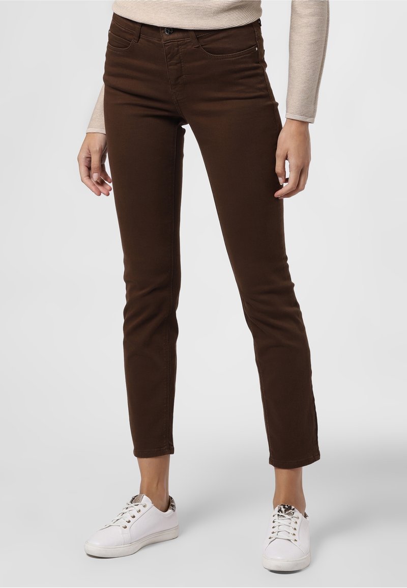 Hnědé slim-fit džíny s středním pasem, se zapínáním na zip a knoflík, předními kapsami a v kombinaci s bílými teniskami.