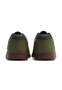 Green athletic shoes with a smooth synthetic upper, textured accents, and brown rubber soles. Features minimal design and reinforced heel.
