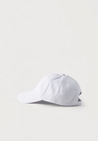 Casquette de baseball en coton blanc posée sur une surface blanche, vue de côté avec la visière orientée vers la gauche.