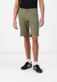 Olive green shorts made of cotton blend fabric, featuring a straight cut, belt loops, and a button closure. Worn with black sneakers.