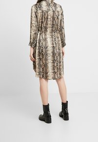 Långärmad klänning med ormtryck, med en insvängt midja, lätt tyg och lös passform. Svarta ankelkängor kompletterar looken.