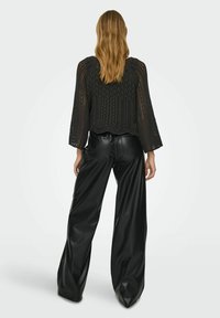 Haut en tricot noir avec des manches évasées ; motif ajouré et ourlet festonné. Associé à un pantalon en faux cuir noir brillant taille haute.