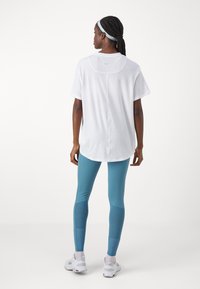 T-shirt atlético branco de mangas curtas, combinado com leggings teal com painéis texturizados e detalhes em azul claro.