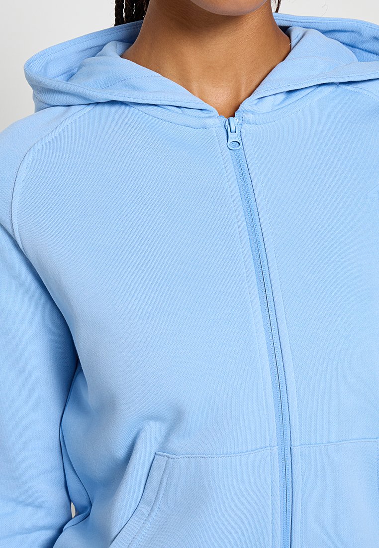 Jasnoniebieska polarowa bluza zapinana na zamek, wykonana z gładkiego materiału, z kapturem, przednimi kieszeniami i subtelnym detalem logo w pobliżu zamka.