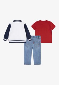 Három ruhadarab: egy fehér és sötétkék dzseki csíkos mandzsettával, egy vörös póló és világoskék farmer hátzsebekkel.