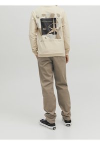 Beige sweatshirt med grafiskt tryck på baksidan, i kombination med ljusbruna byxor. Svarta sneakers fulländar outfiten, med en logotyp på skon.