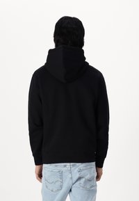 Haut à capuche noir avec une grande capuche, doté d'une coupe décontractée et de manches longues. Assorti à un jean bleu clair avec des détails de couture subtils.