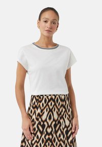 T-shirt blanc à manches courtes avec un col rayé noir et blanc, associé à une jupe à motifs avec des formes de losanges en marron et crème.
