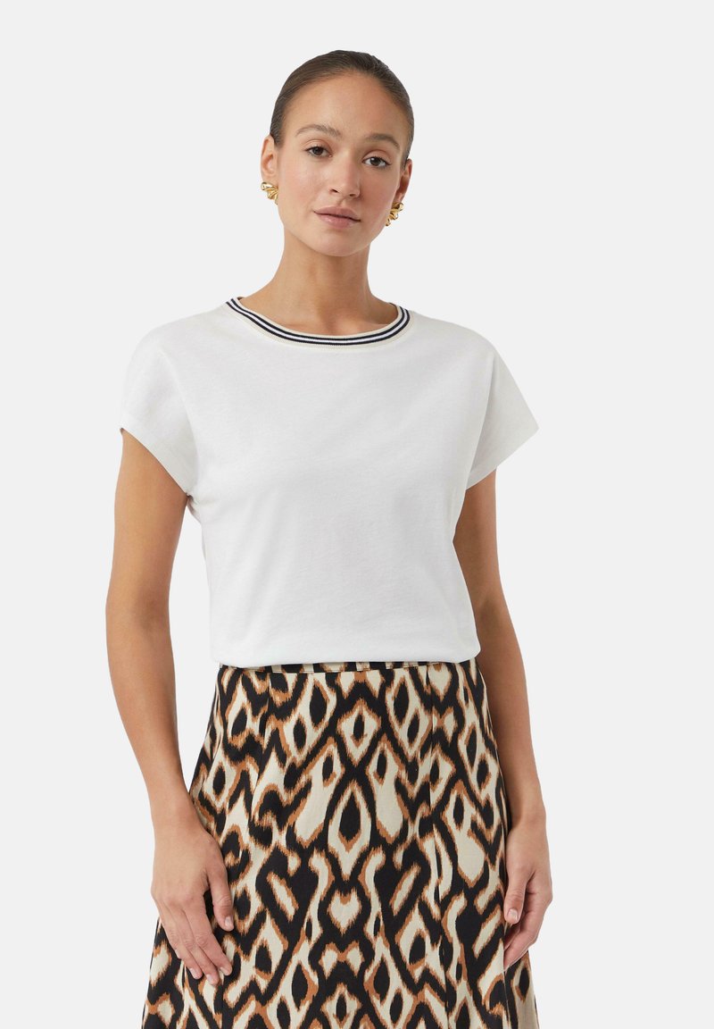 T-shirt blanc à manches courtes avec un col rayé noir et blanc, associé à une jupe à motifs avec des formes de losanges en marron et crème.