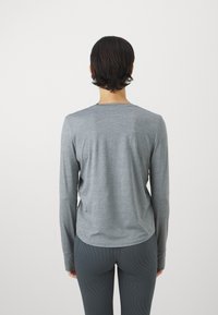 Pitkähihainen harmaa paita pyöreällä kaula-aukkolla, tehty sileästä kankaasta. Suora leikkaus ja sivuhiusleikkaus. Yhdistetty kuvioituihin legginsseihin.