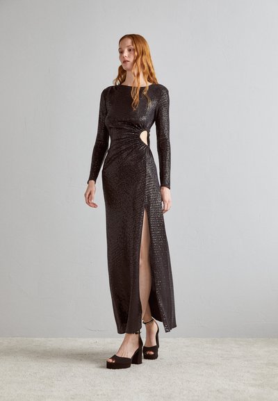 Abito nero con paillettes e maniche lunghe, dotato di uno spacco laterale e dettaglio a taglio in vita, abbinato a tacchi a piattaforma spessi.
