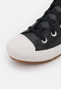 Sneaker nera con una punta bianca texturizzata e rigata, lacci neri e occhielli argentati; presenta una suola in gomma naturale.