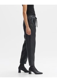 Czarne dresowe spodnie z ekoskóry z elastycznym paskiem w talii, zwężanymi nogawkami i bocznymi kieszeniami. Stylizowane z czarnymi botkami na obcasie.