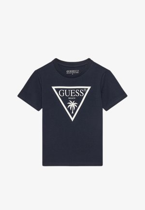 T-shirt in cotone biologico blu navy con maniche corte, caratterizzata da un logo triangolare bianco con la scritta "GUESS BEACH" e un'immagine di palma.