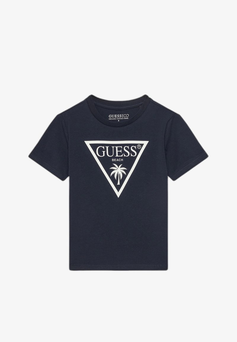 T-shirt en coton biologique bleu marine à manches courtes, avec un logo triangle blanc affichant "GUESS BEACH" et un graphique de palmier.