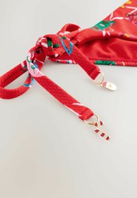 Piros bikini felsőrész texturált pántokkal, virágmintával. Arany színű zárók csatokkal, amelyek karácsonyi témájú díszítéssel vannak ellátva.