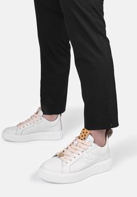 Sneaker bianche con suole crema testurizzate, lacci pesca e un accento lavorato in beige sul tallone. Indossate con pantaloni neri a tubo.