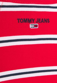 Czerwona bawełniana koszula z poziomymi paskami w kolorze białym i granatowym. Posiada haftowane logo "TOMMY JEANS" oraz małą akcentującą aplikację poniżej.