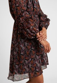 Robe à imprimé floral avec manches bouffantes, taille cintrée, en tissu foncé agrémenté de feuilles orange, rose et vertes. Ourlet transparent à couches avec rayures.