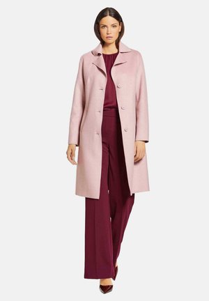 Light pink coat with a notched collar, five buttons, and a straight cut. Worn over a deep burgundy outfit and high-heeled shoes.