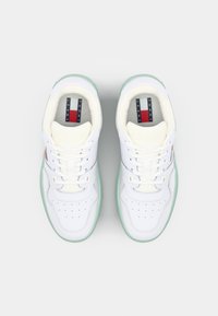 Baskets en cuir blanc avec semelles vert menthe, présentant des détails perforés, des lacets blancs et un logo Tommy Jeans sur la semelle intérieure.