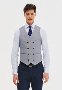 Szary kamizelka w paski z sześcioma guzikami, czarnymi akcentami i dwoma kieszeniami z przodu. Nosi się ją na białej koszuli i zestawia z niebieską krawatem.