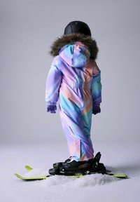 Ski odijelo u pastelnim nijansama ljubičaste, plave i ružičaste boje s kapuljačom obrubljenom krznom. Crni šešir i rukavice, prikladno odjeveno na skije s zelenim detaljima.