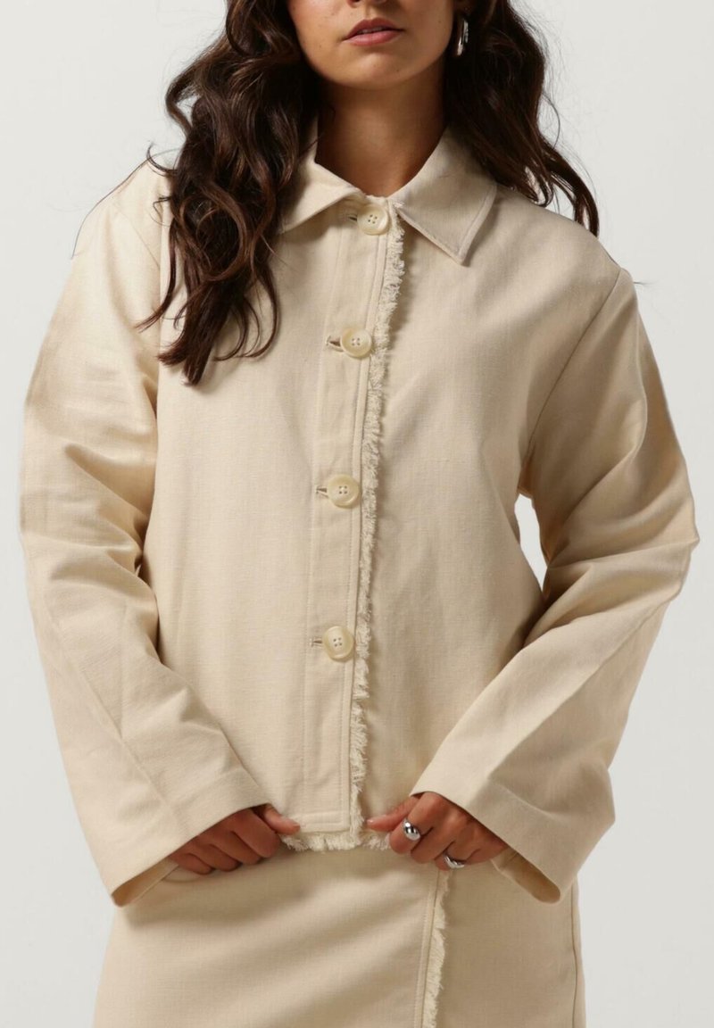 Beige cropped jasje met een spitse kraag, knoopsluiting en rafelige zoom. Gemaakt van textiel met een structuur en lange mouwen.