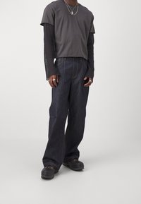 Dark denim wide-leg jeans with visible stitching, paired with a gray short-sleeve top over a long-sleeve black shirt. Chunky footwear.