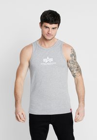 Grå ärmløs tank topp med rund halslinning og hvit "Alpha Industries" logo på brystet; tettsittende design; myk bomullsblanding.